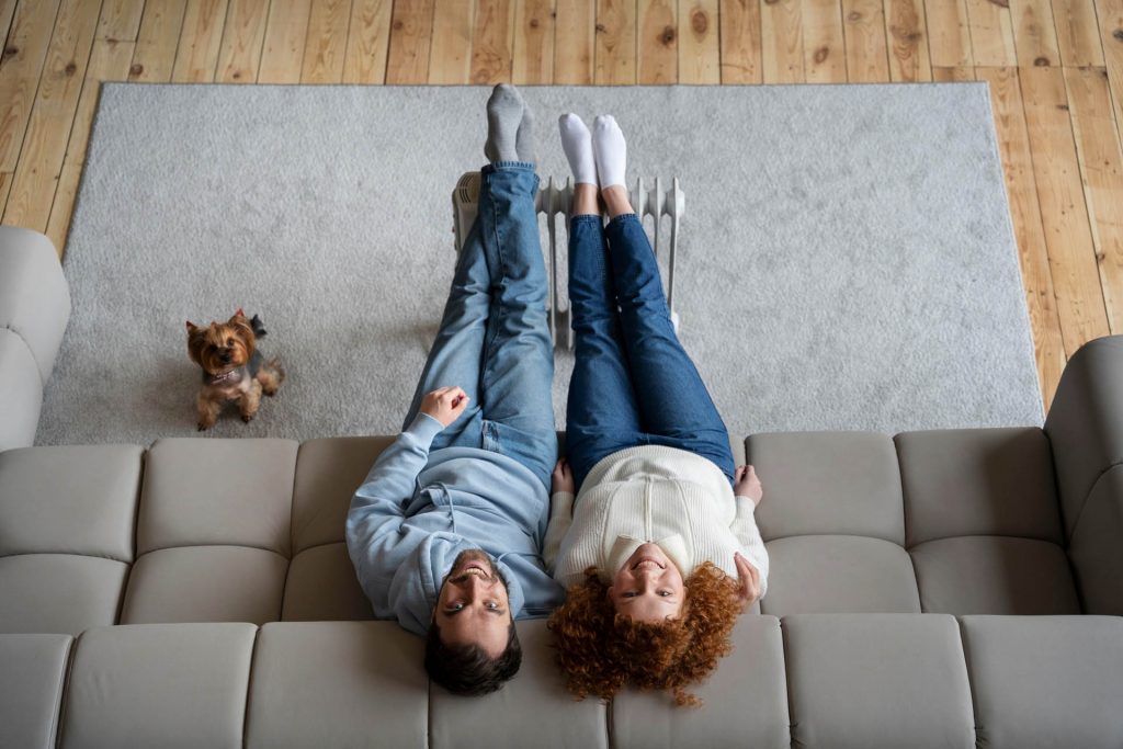 Smiling happy and Young couple on couch looking up at their Mini Split HVAC on the wall after heating contractor in Manchester nh - Elite Heating and Cooling